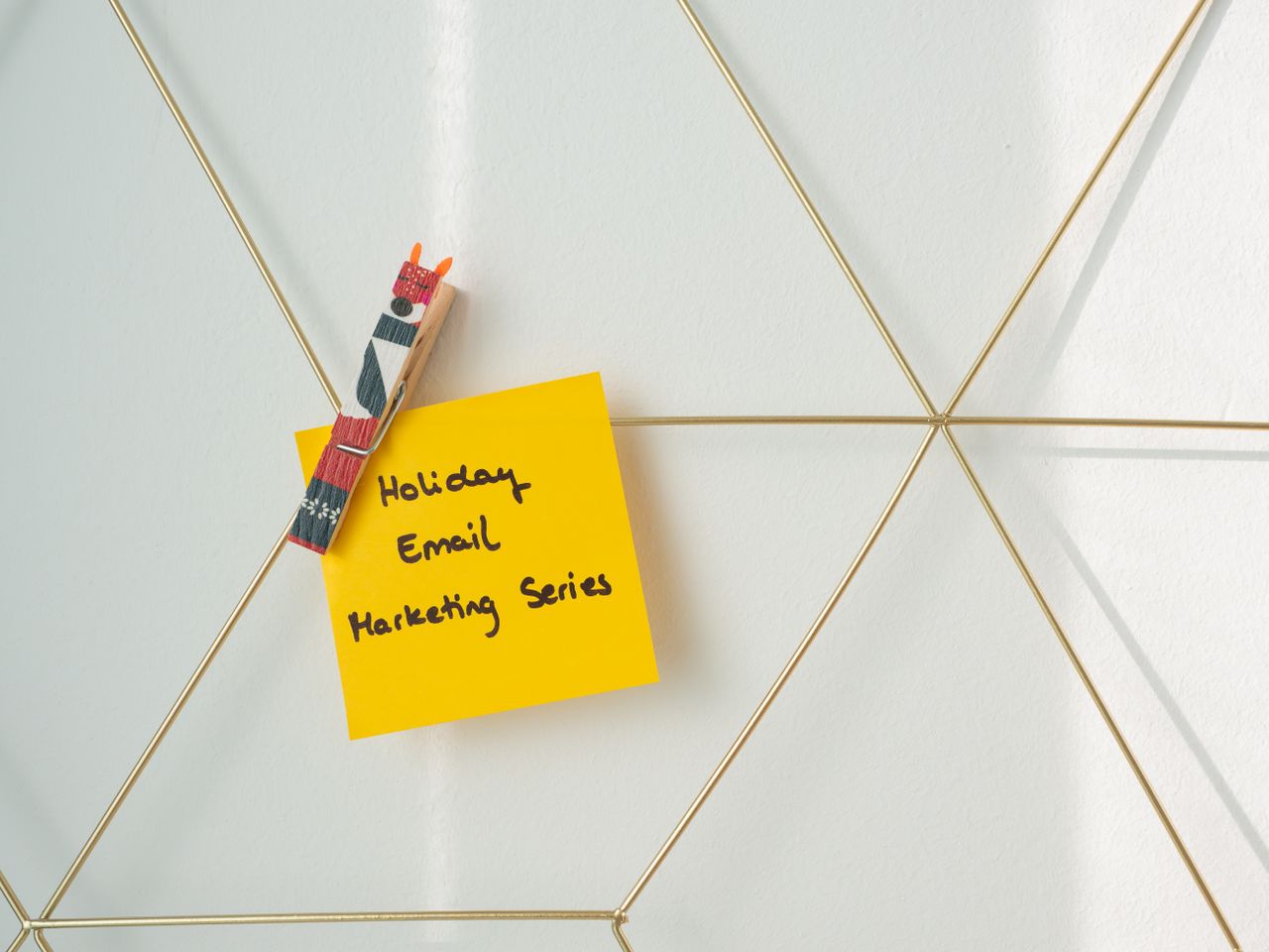 Post-it jaune vif avec un message de marketing par e-mail pour les fêtes, fixé sur un mur en grille métallique.